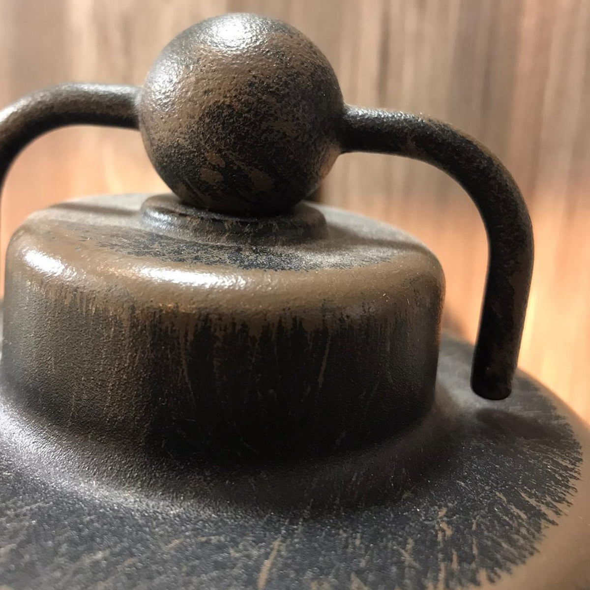 Close-up of a rustic, dark metal lantern top with a spherical finial and curved handle.