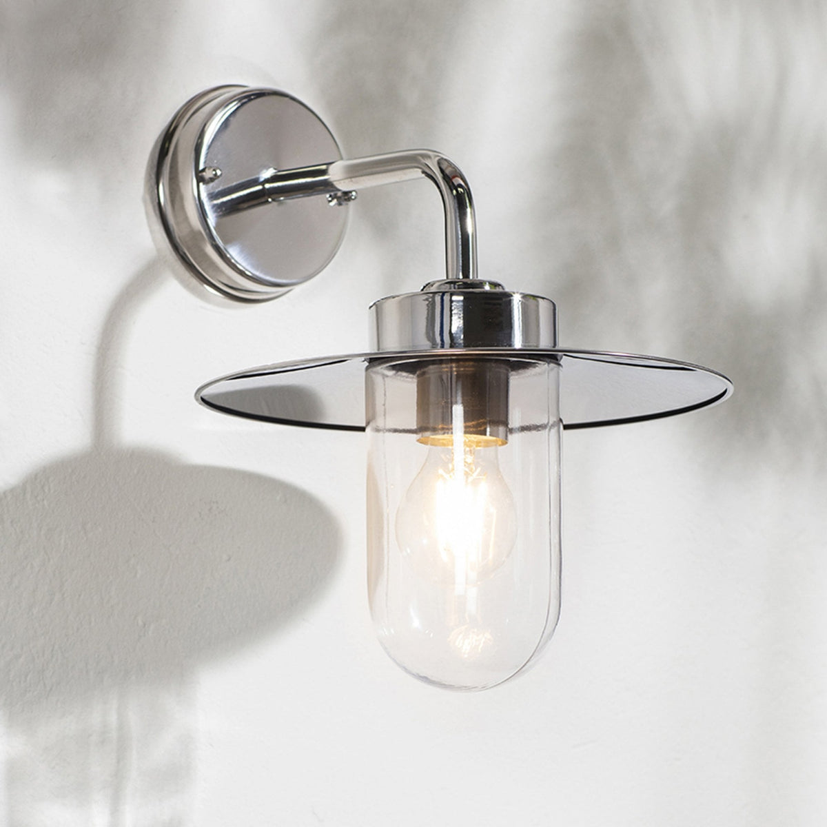 Polished chrome wall light with a clear glass shade and a wide, flat metal top.