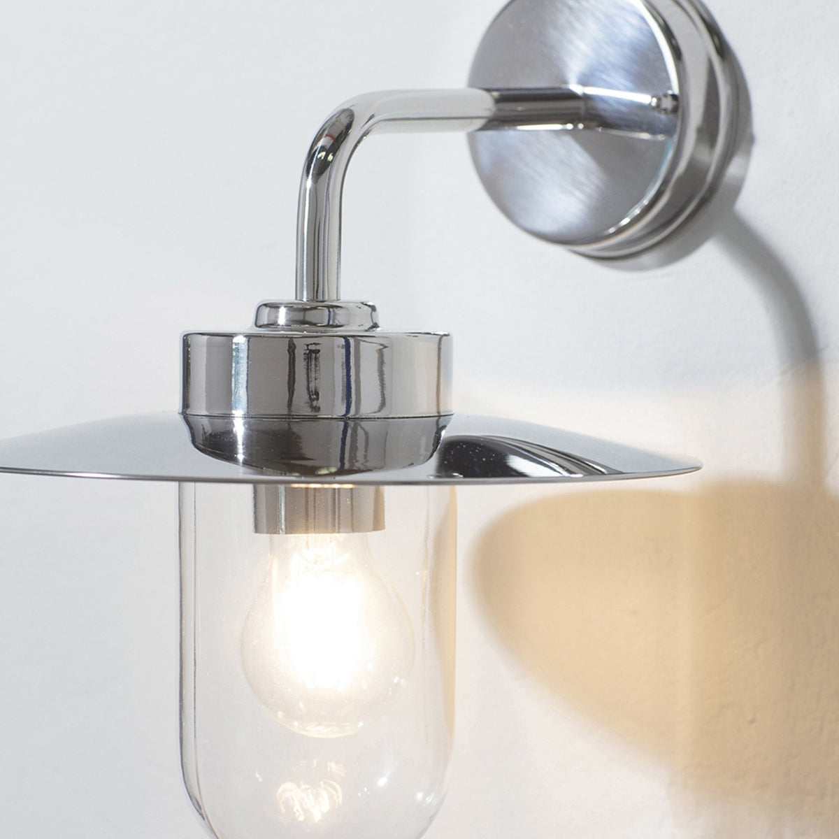 Close-up of a polished chrome wall light with a clear glass shade and a wide, flat metal top.