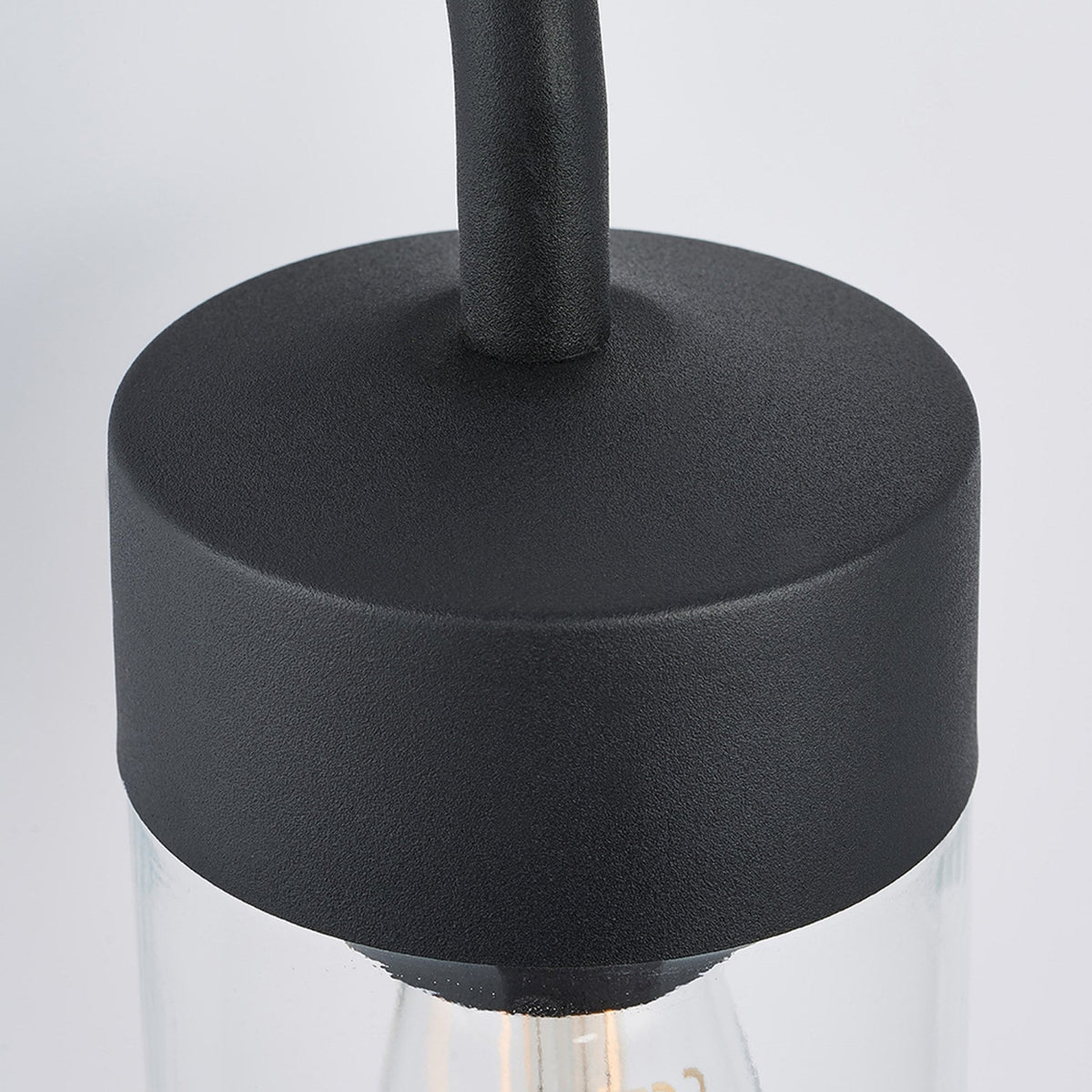 Close-up of the black top cap and clear glass shade of an outdoor wall light.