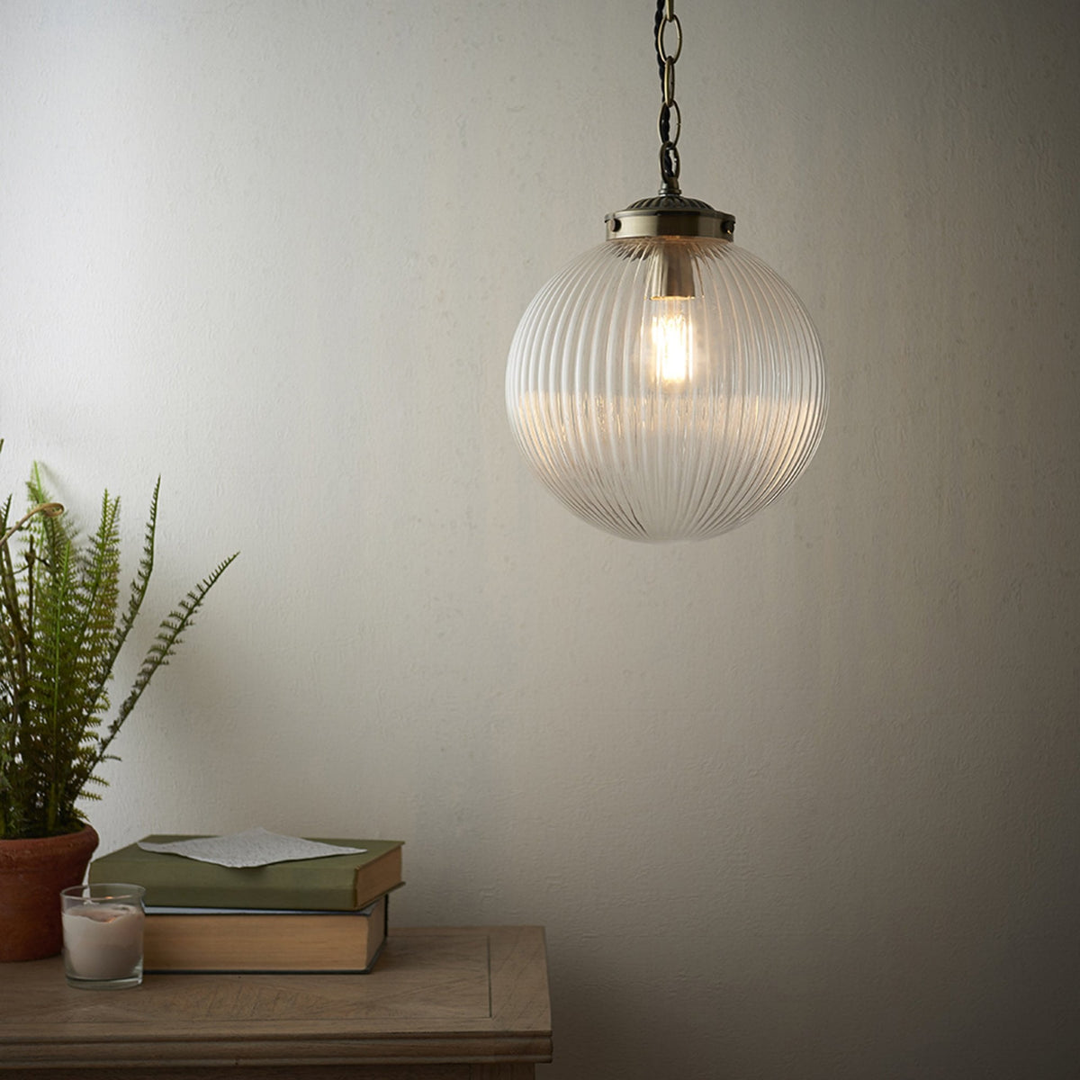 Ribbed glass pendant light with a brass fixture, illuminating a corner with a potted plant and books.
