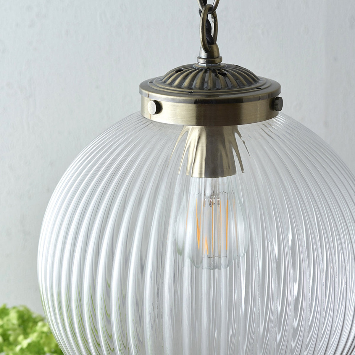 Close-up of a ribbed glass globe pendant light with a brass fixture and an exposed filament bulb.