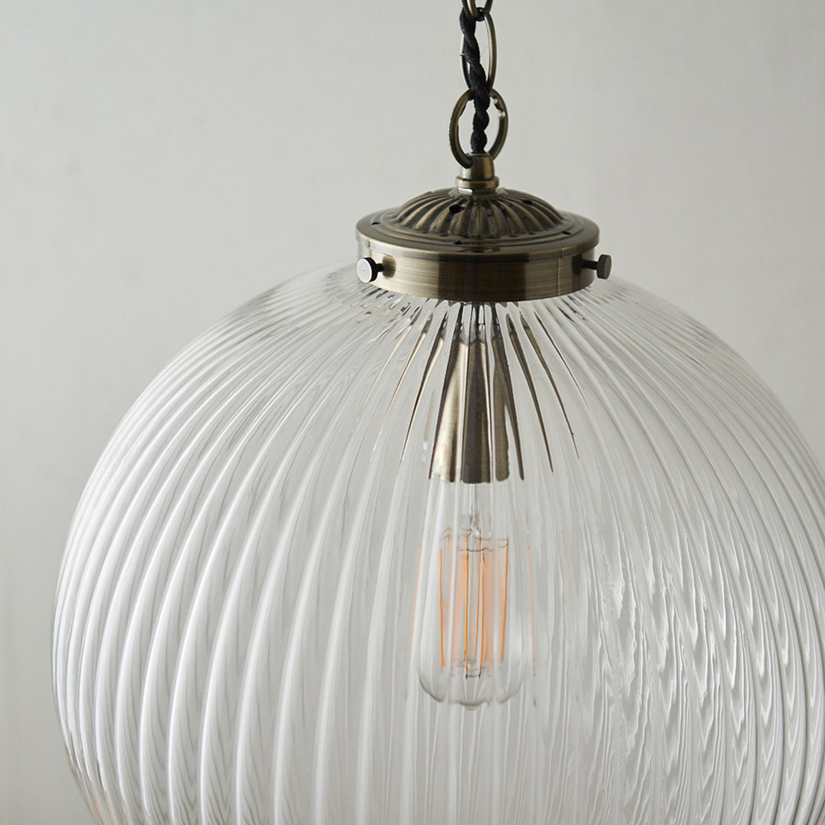 Close-up of a ribbed glass globe pendant light with an antique brass fitting and an exposed filament bulb.