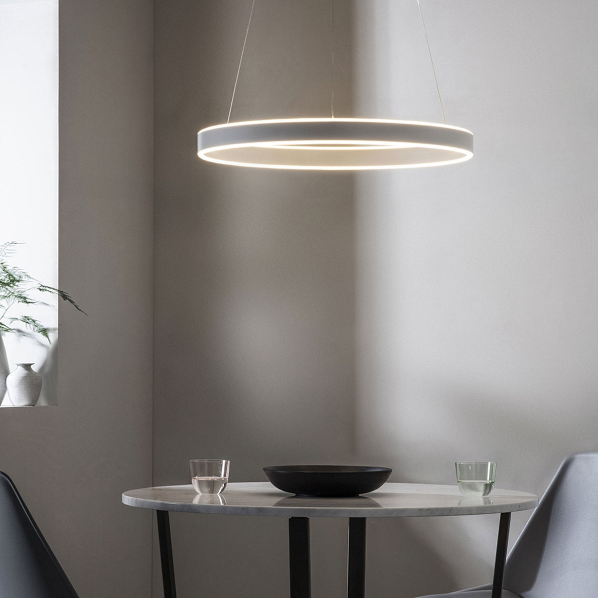Modern circular LED pendant light illuminating a dining table with a bowl and two glasses.