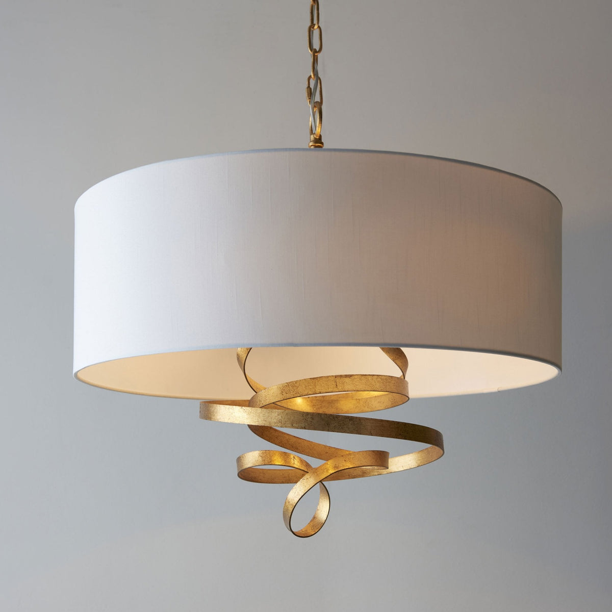 A close-up view of the pendant light reveals its textured gold metal ribbons and white fabric drum shade.