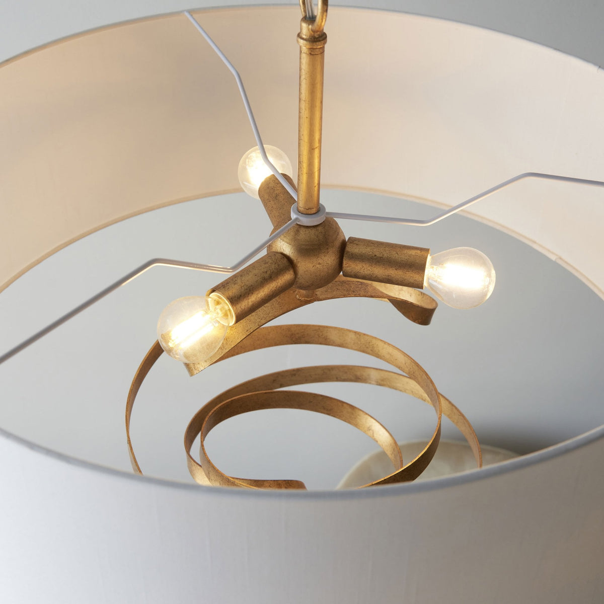 A close-up view shows the three bulbs and the metallic gold ribbon design inside the pendant light's shade.
