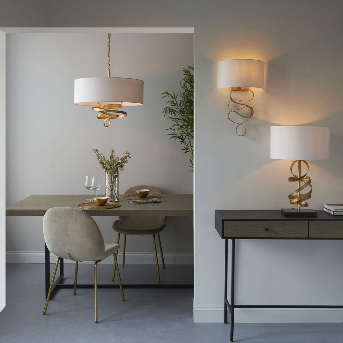 A dining room features the pendant light, alongside matching wall and table lamps with golden ribbon designs.