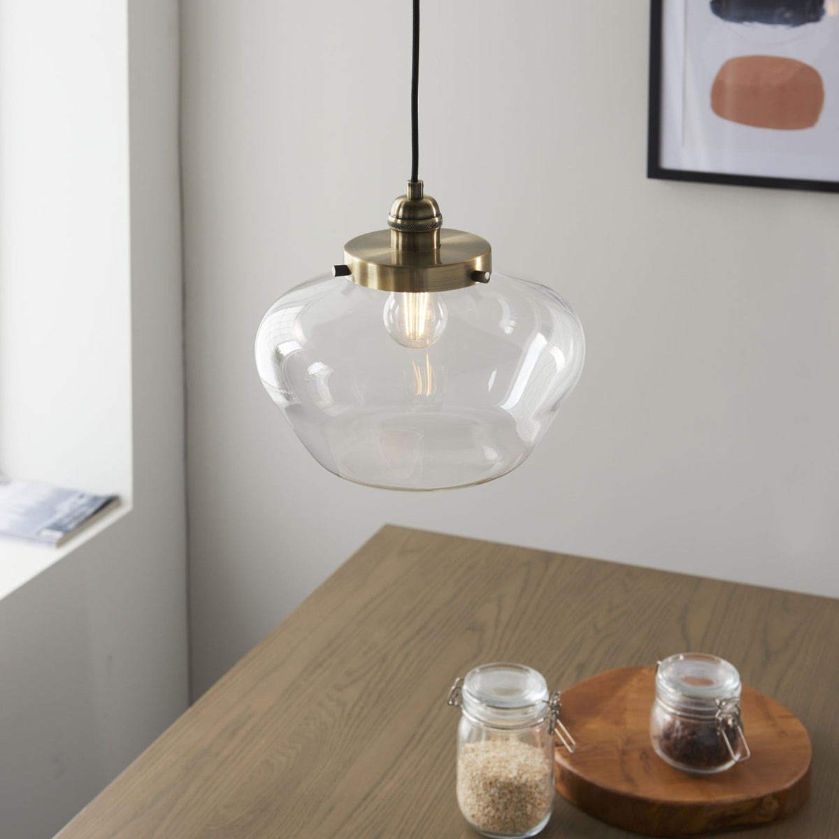 Clear glass pendant light hanging above a wooden dining table with jars and a framed picture.