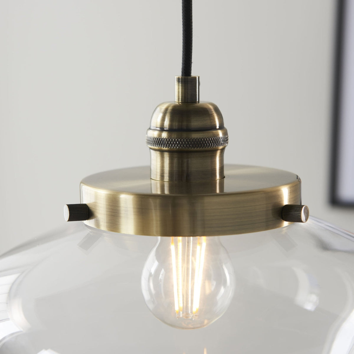 Detailed view of the brass fitting and exposed filament bulb within the clear glass pendant light.