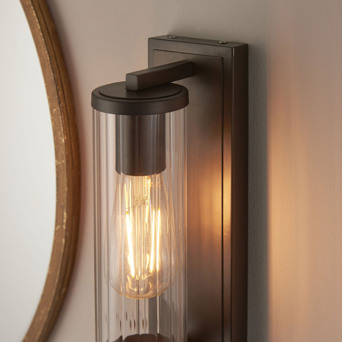 Close-up of a bronze wall light with a clear ribbed glass shade and an exposed filament bulb.