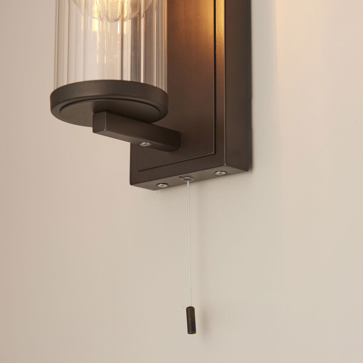 Bottom view of a bronze wall light with a clear ribbed glass shade and a pull cord switch.