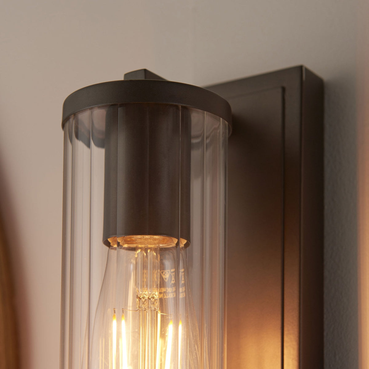 Top view of a bronze wall light with a clear ribbed glass shade and an exposed filament bulb.