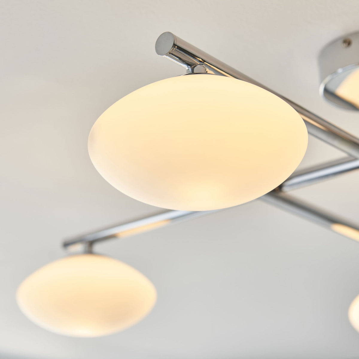 Close-up of one opal glass shade on a four-light ceiling fitting with chrome finish.