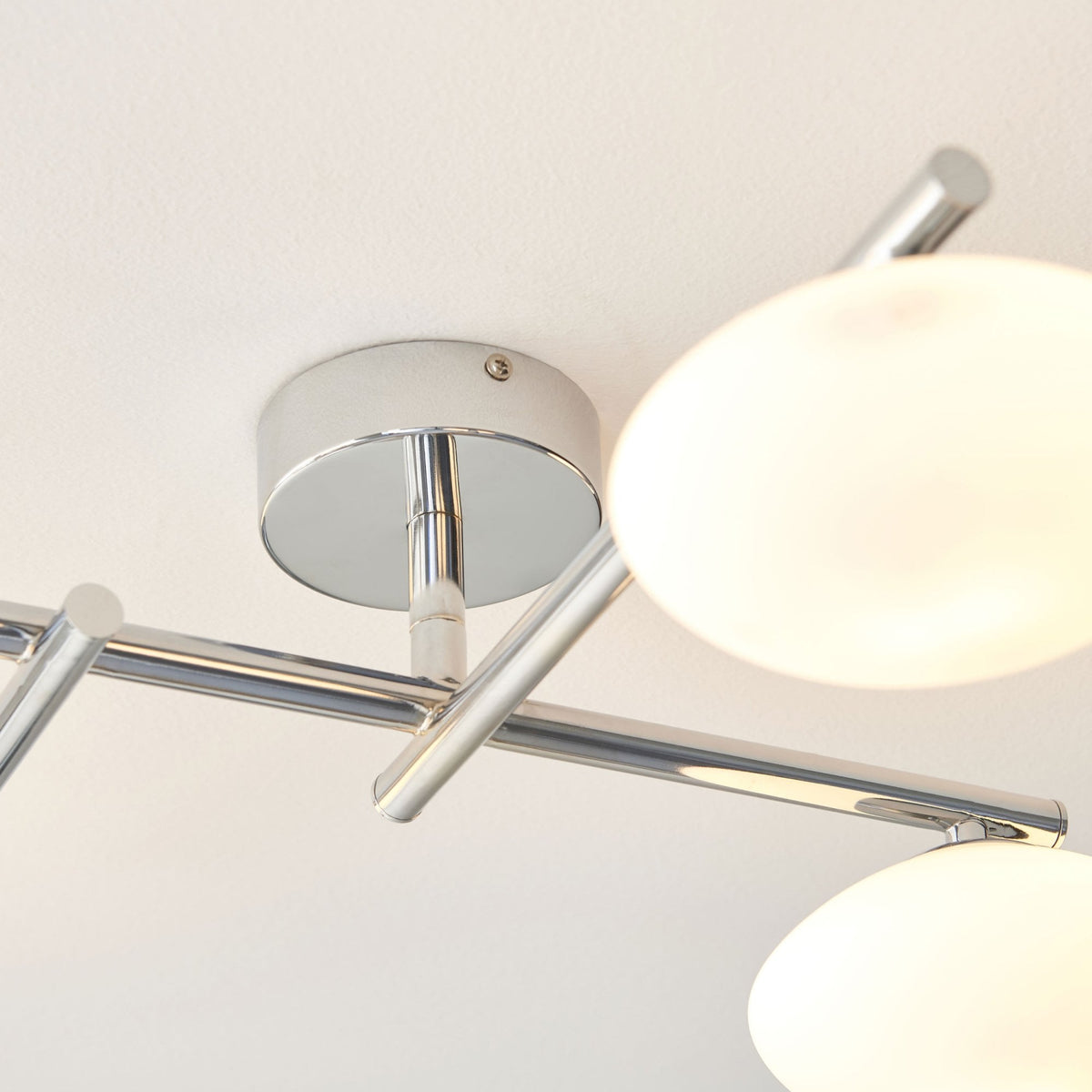 Close-up of the chrome base and one opal glass shade of a four-light ceiling fitting.