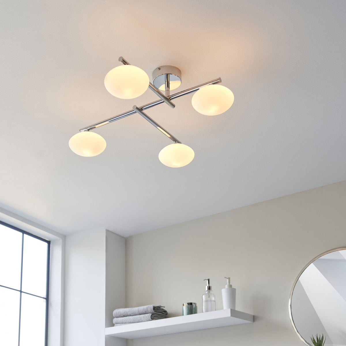 Four-light ceiling fitting with chrome finish and opal glass shades illuminating a bathroom.