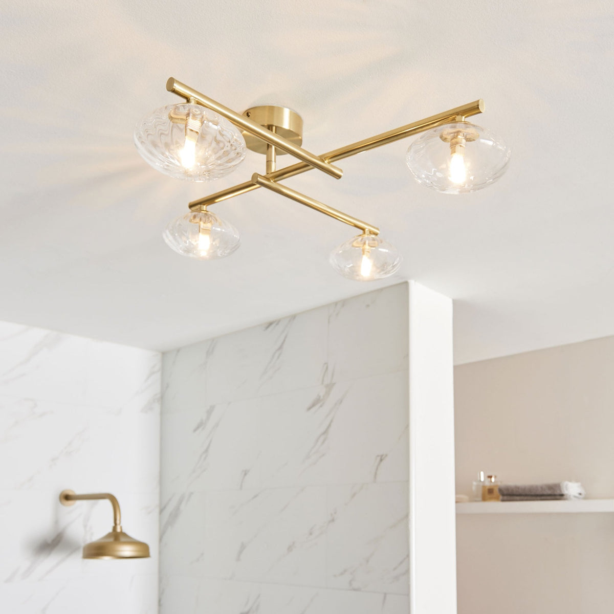 Four-light ceiling fixture with clear glass shades and brass arms in a bathroom.