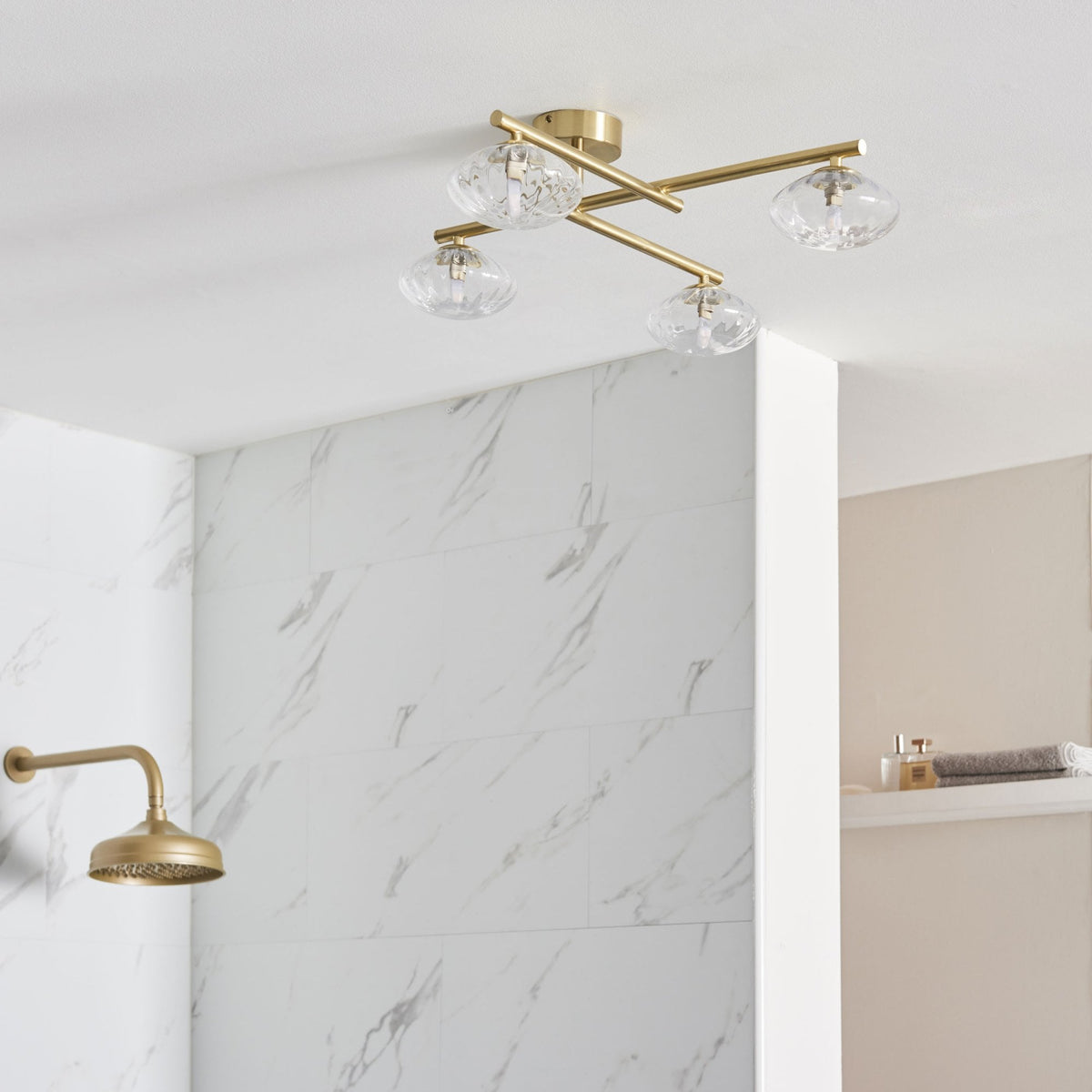 Four-light ceiling fixture with clear glass shades and brass arms in a bathroom.