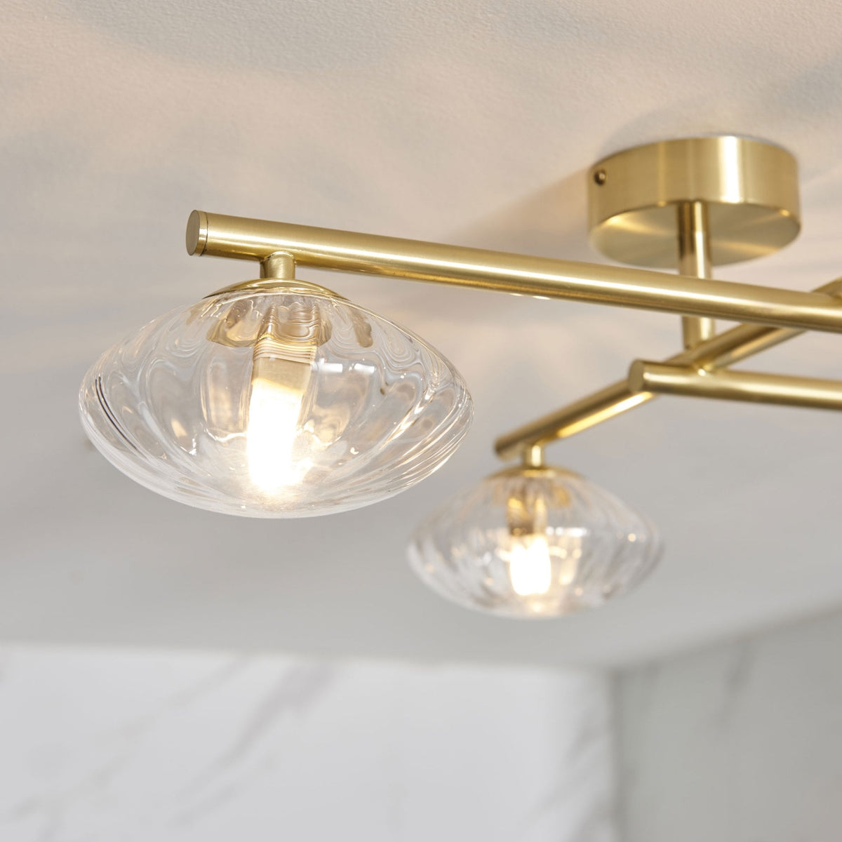 Close-up of a four-light ceiling fixture with clear glass shades and brass arms.