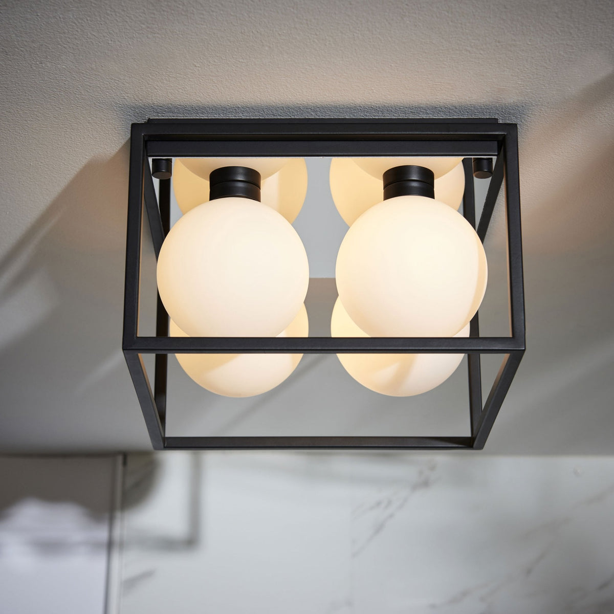 A modern black square ceiling light with four white globe bulbs, illuminating a white ceiling.