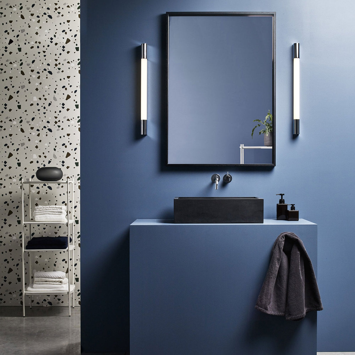 Bathroom with blue walls, black sink, mirror, and white shelving unit with towels