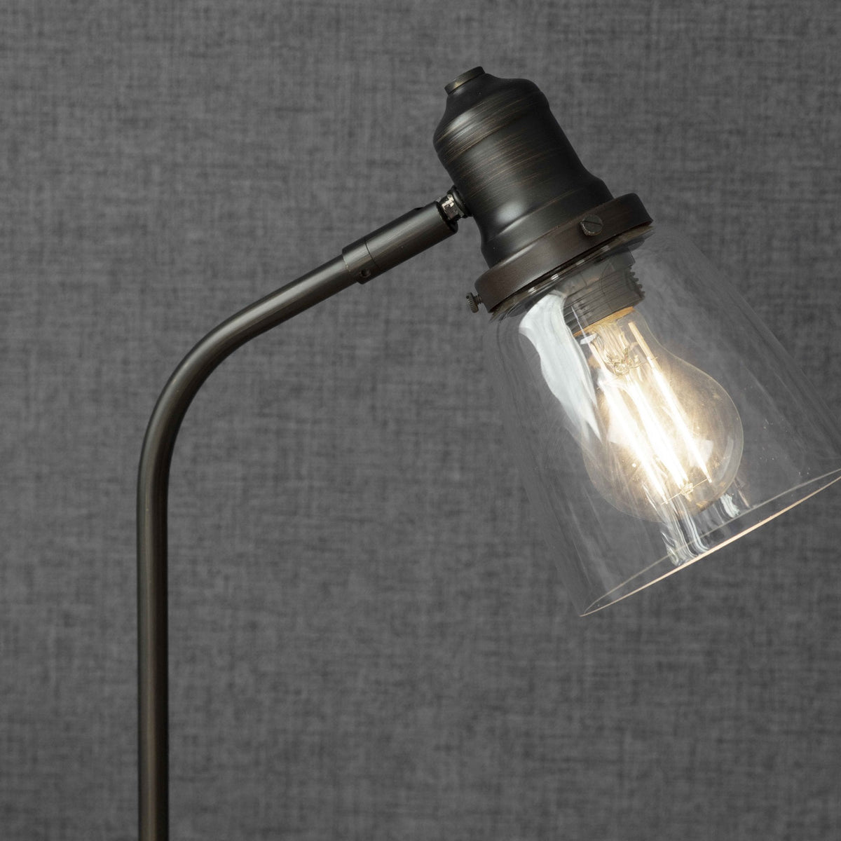 Close-up of a bronze desk lamp with a clear glass shade and an illuminated Edison bulb.