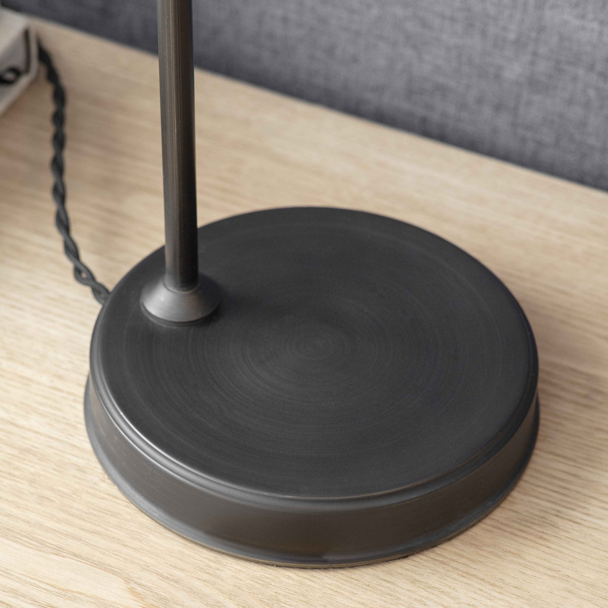 Close-up of a dark bronze lamp base with a braided cord on a light wood surface.