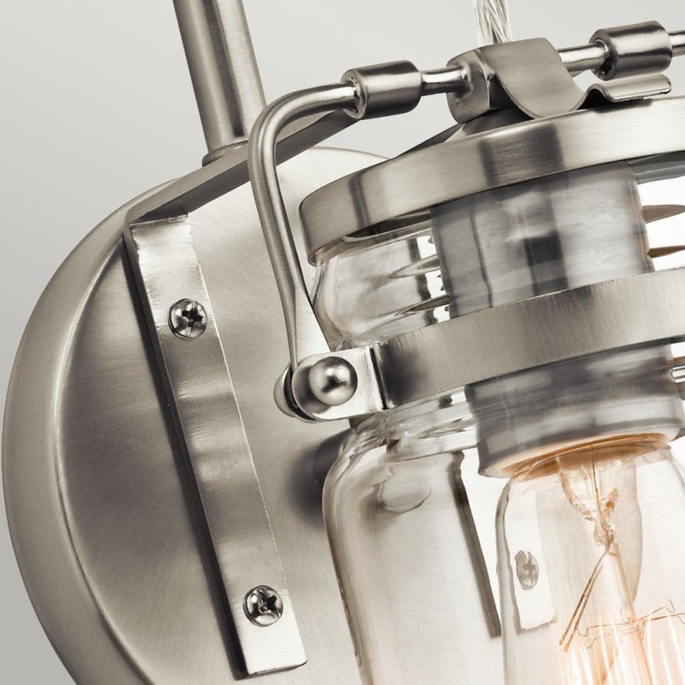 A detailed view of the brushed nickel mounting plate and arm of a wall sconce.