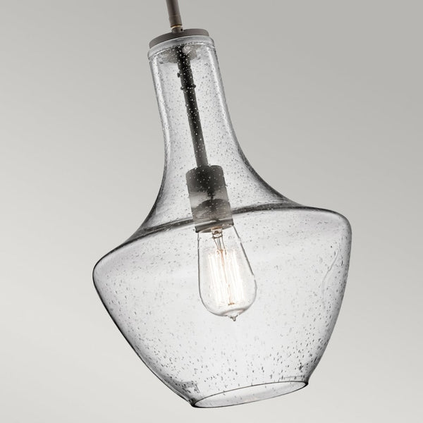 Close-up of the clear seeded glass shade and exposed bulb of the bronze pendant light.