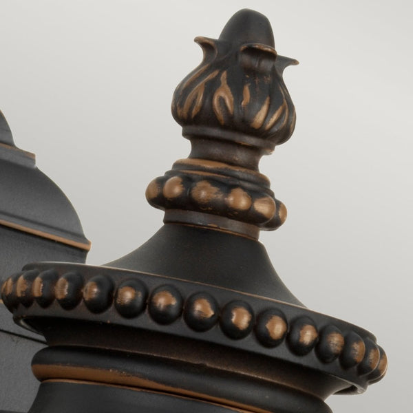 Close-up of the ornate top finial on the outdoor wall light, showcasing antique bronze details.