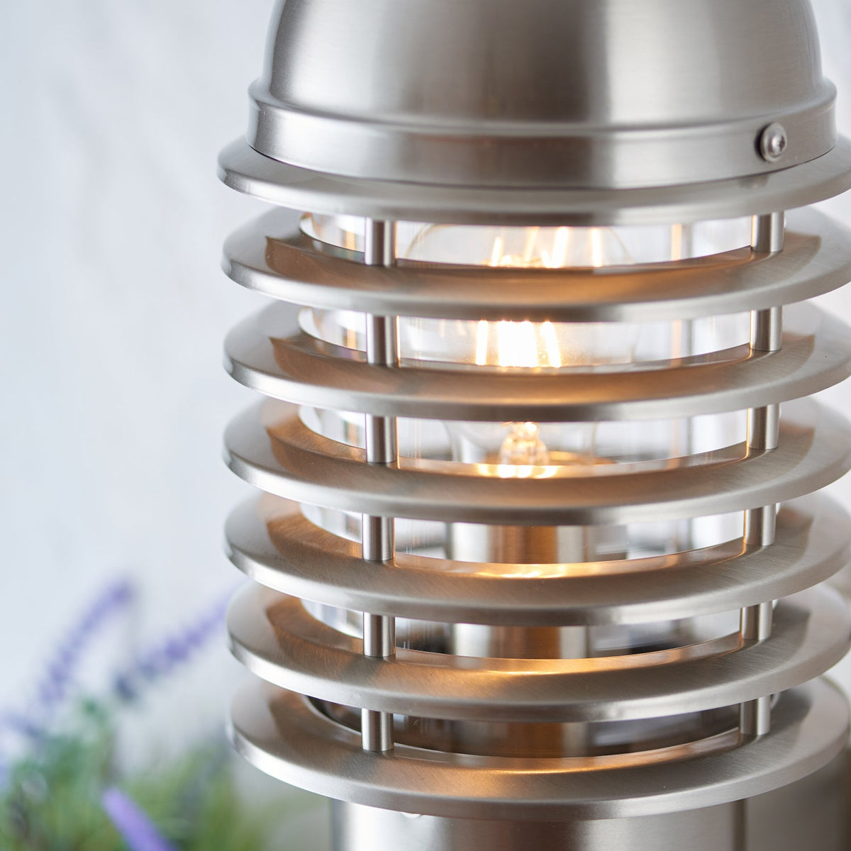 Close-up of a brushed stainless steel outdoor wall light with a warm glowing bulb.
