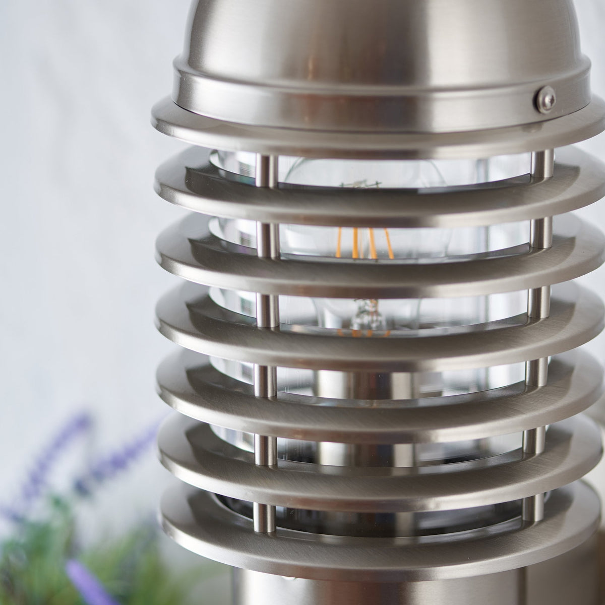 Close-up of a brushed stainless steel outdoor wall light with an unlit bulb.