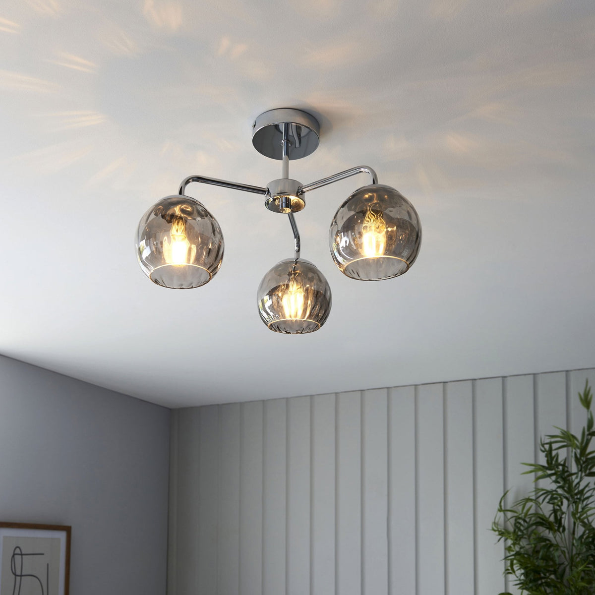 Chrome ceiling light with three smoked glass shades, illuminating a room with light grey paneled walls.