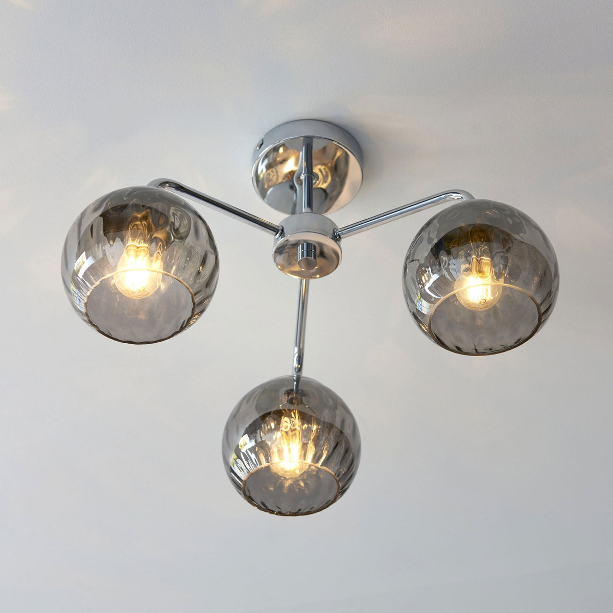 Chrome ceiling light with three smoked glass shades, casting light patterns on a white ceiling.