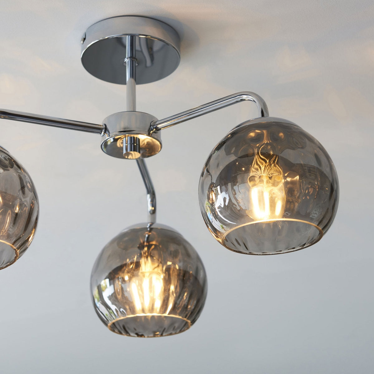 Chrome ceiling light with three smoked glass shades, showing two shades with illuminated bulbs.