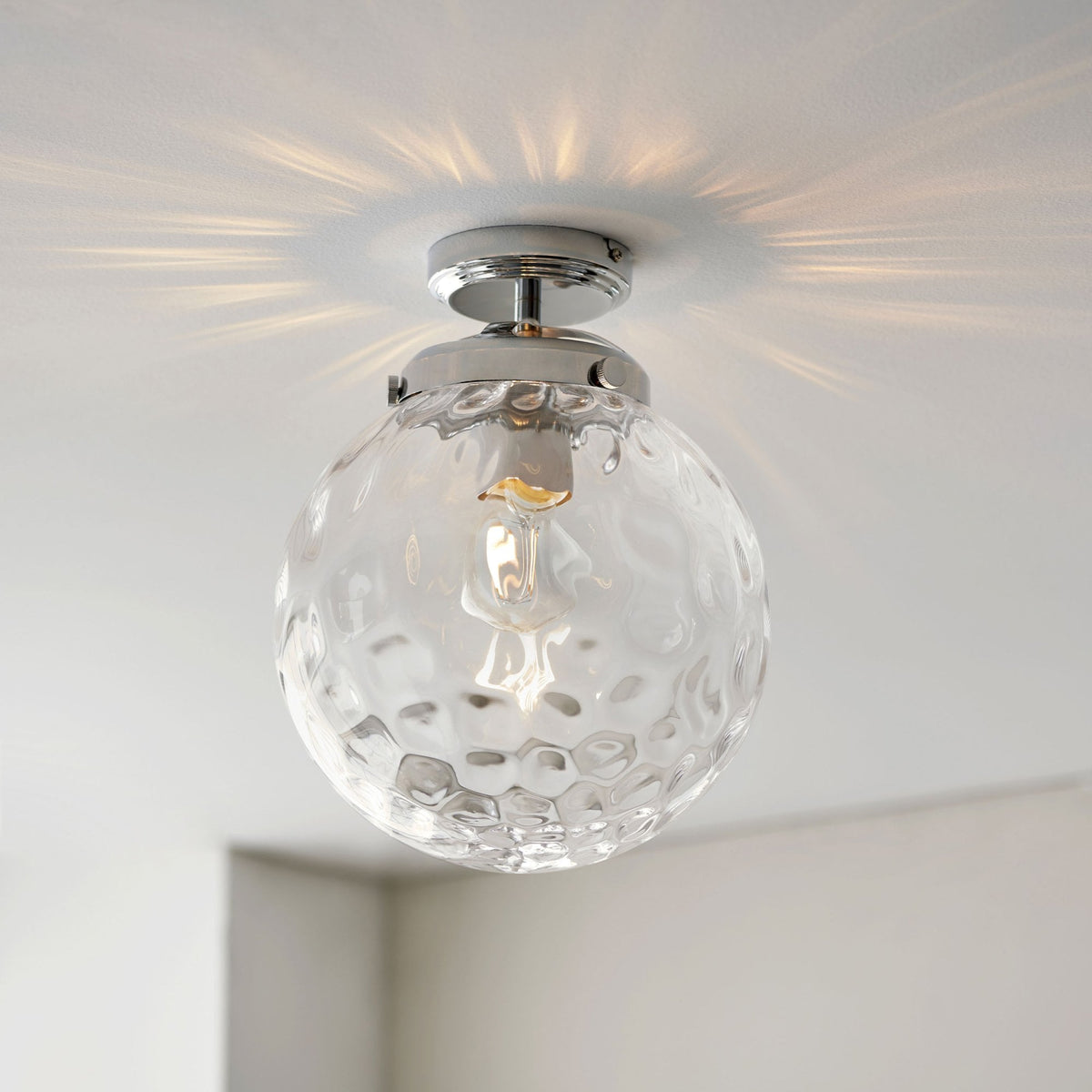 A clear, textured glass globe ceiling light with a chrome base illuminates a white ceiling.