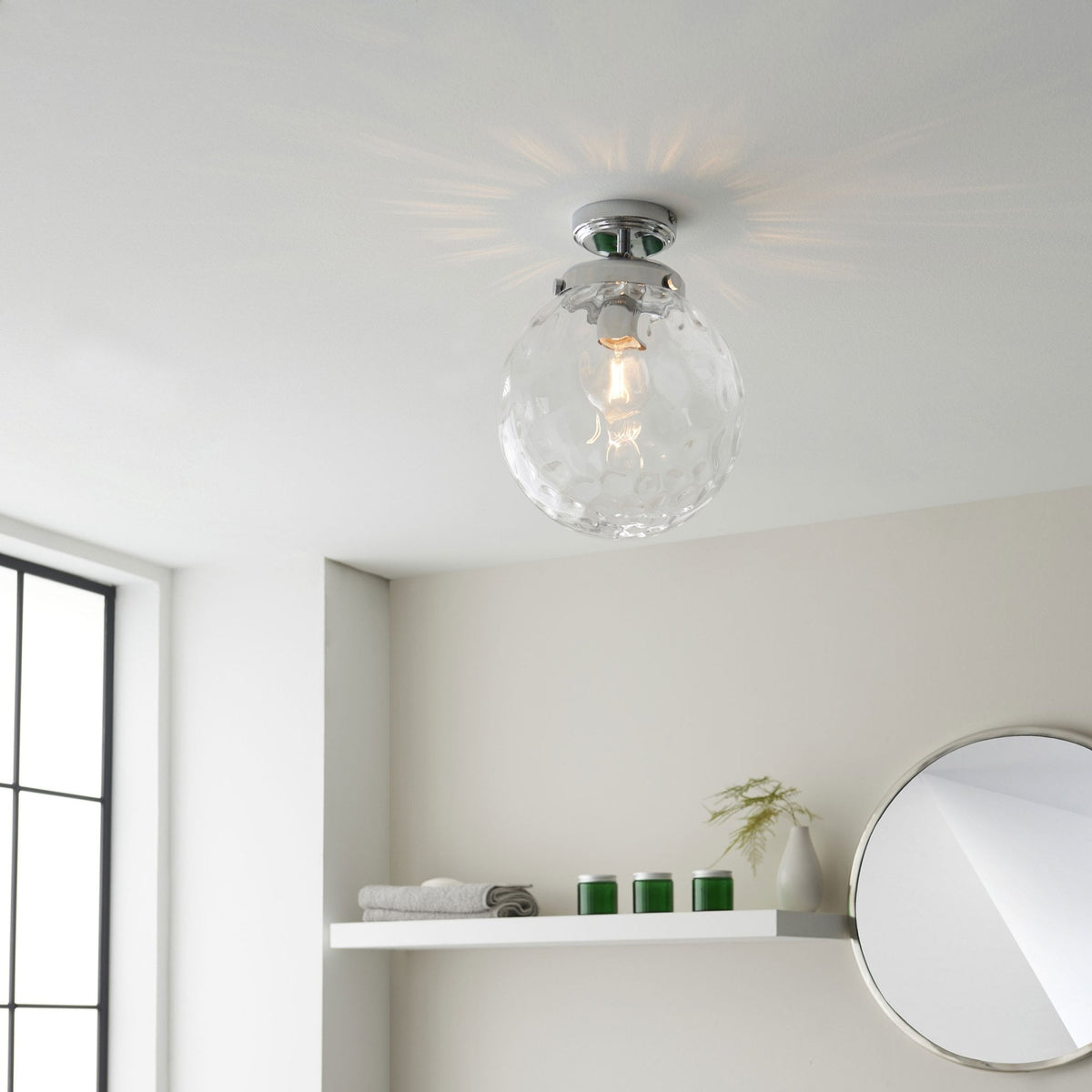 A clear, textured glass globe ceiling light with a chrome base illuminates a modern room.