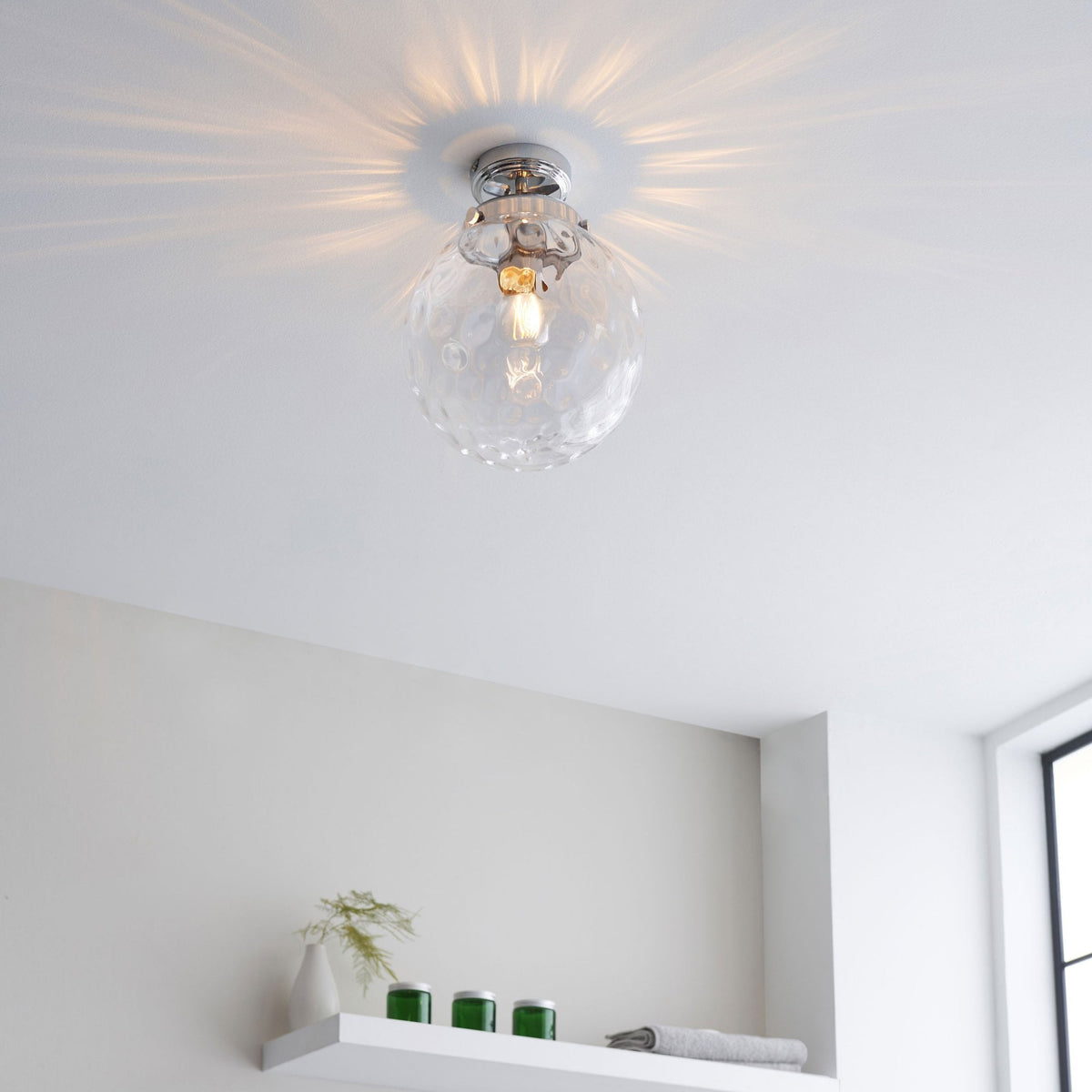 A clear, textured glass globe ceiling light with a chrome base illuminates a modern room from a distance.