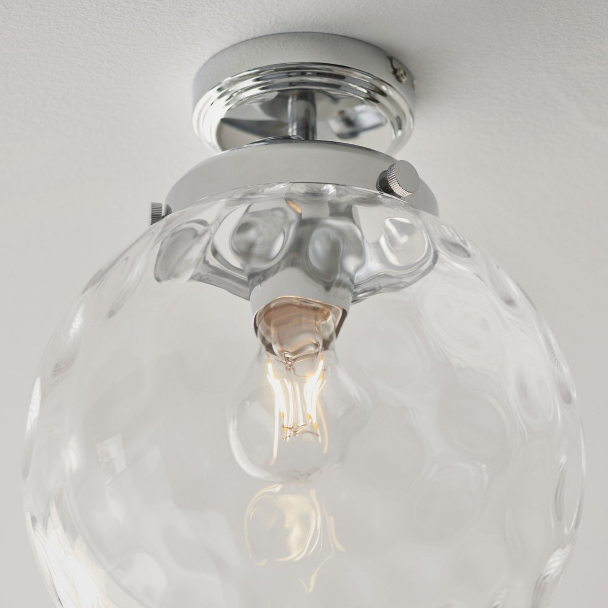 Close-up of a clear, textured glass globe ceiling light with a chrome base.