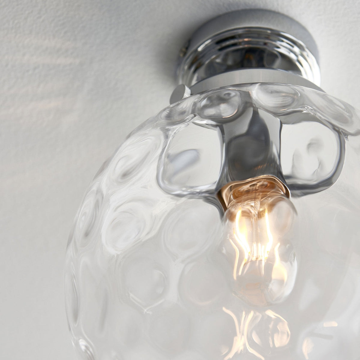 Close-up of a clear, textured glass globe ceiling light with a chrome base.