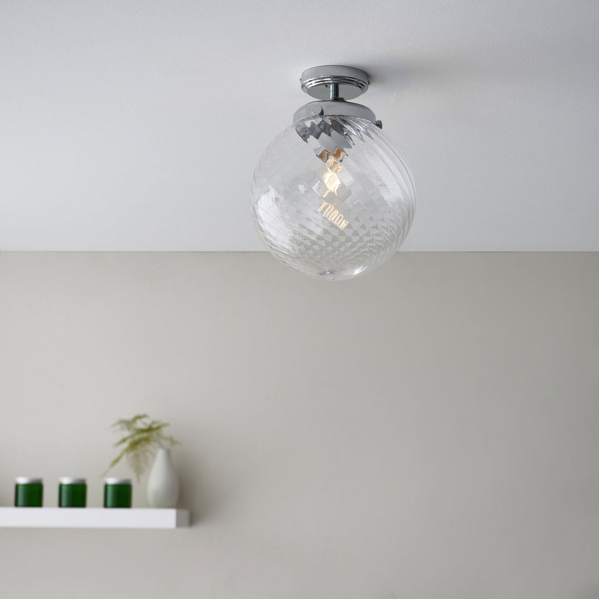 Clear glass globe ceiling light with a chrome base and a swirling pattern, in a room with a white shelf.