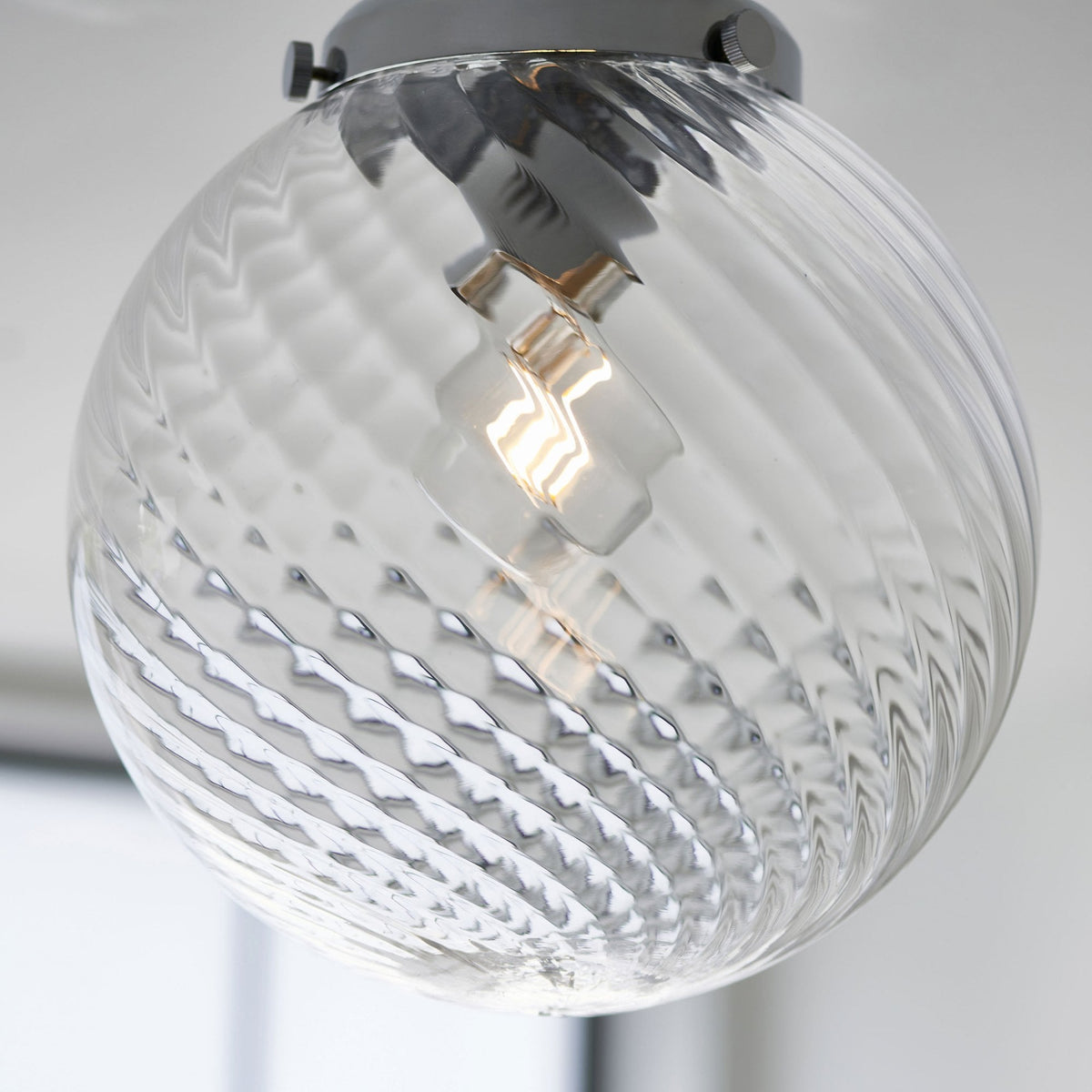 Close-up of a clear glass globe ceiling light with a chrome base and a swirling pattern on the glass.