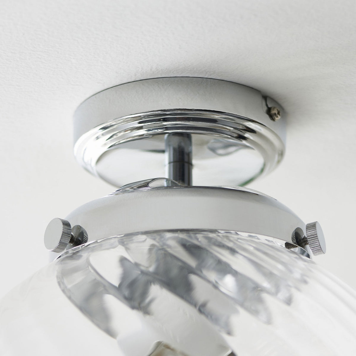 Close-up of the chrome base of a clear glass globe ceiling light.