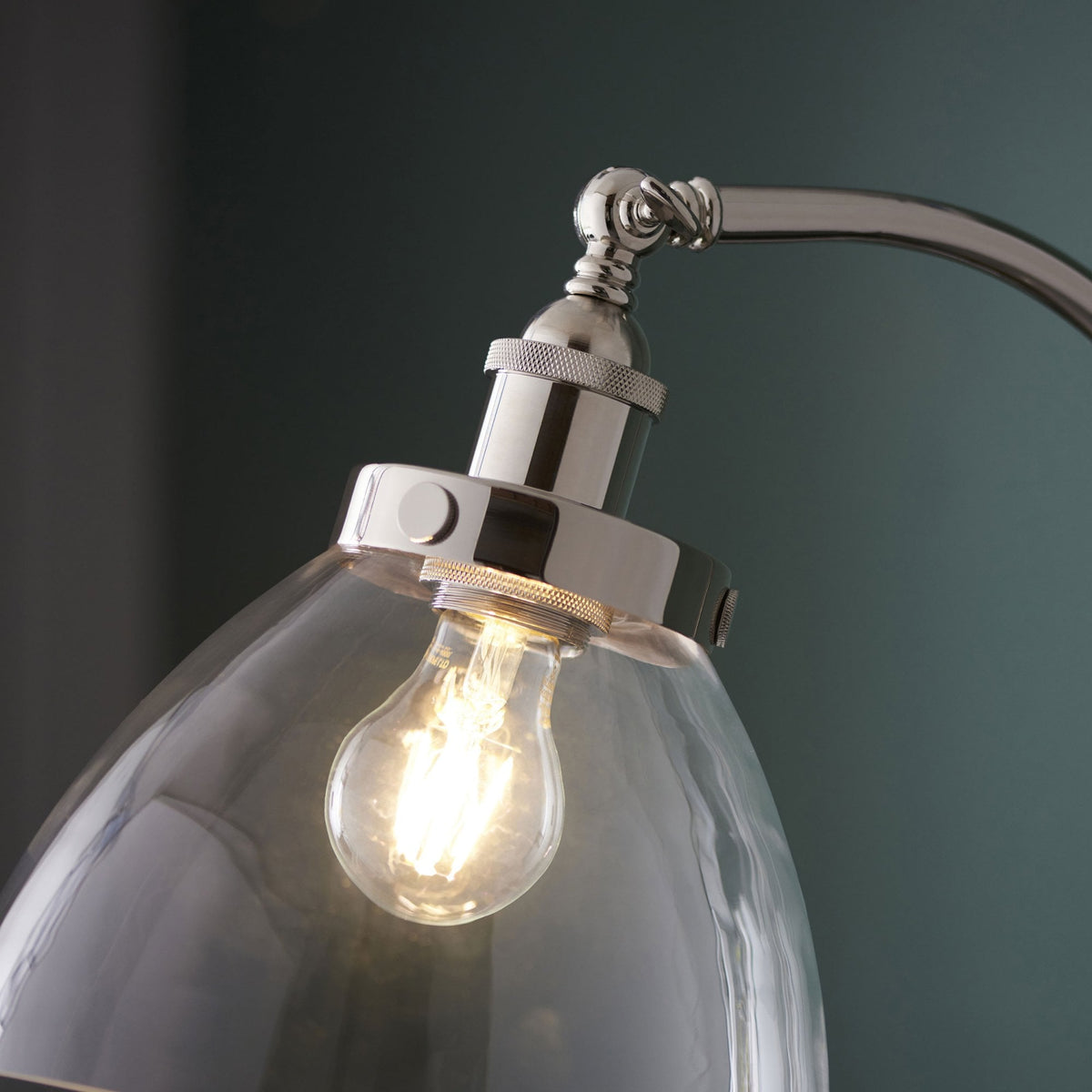 Close-up of the lamp's clear glass shade, showing the illuminated bulb and polished silver fittings.