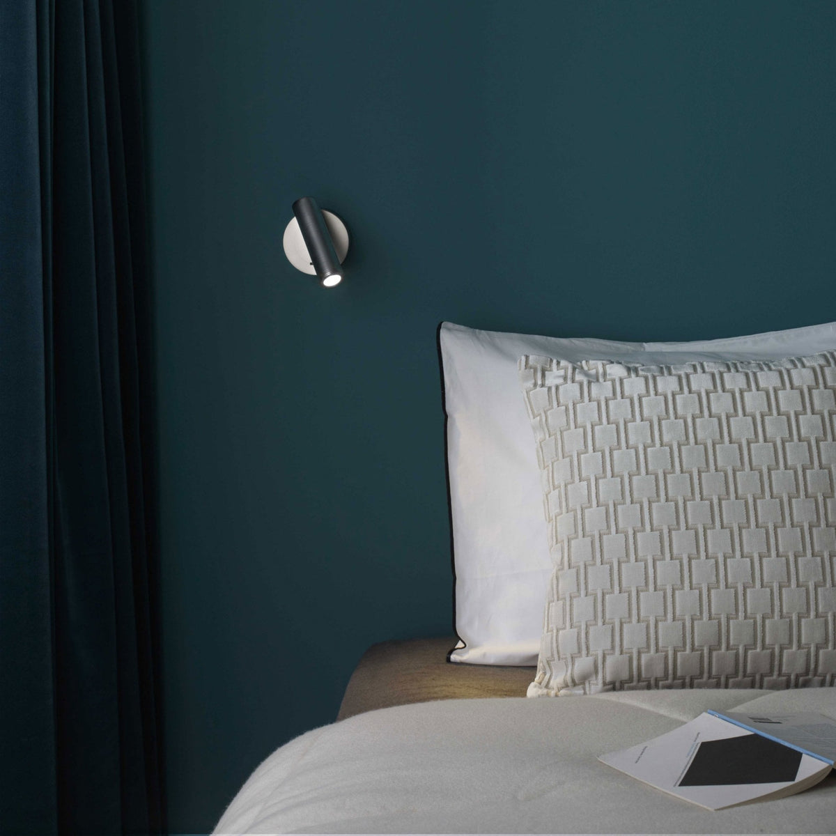 Wall-mounted reading light above a bed with patterned pillows and a book