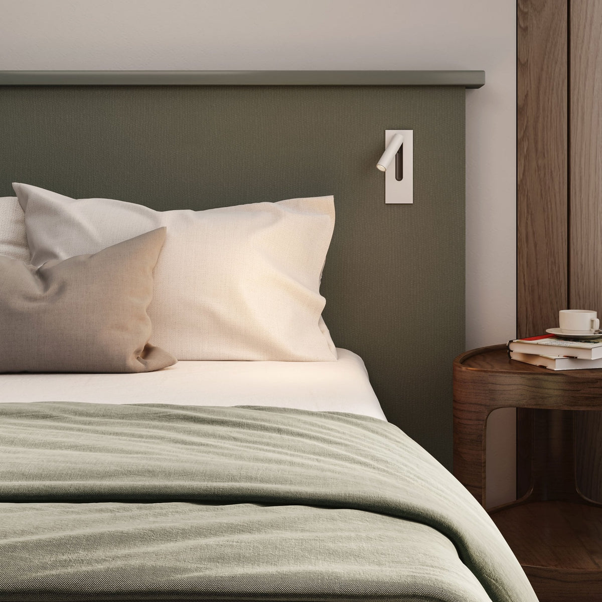 Bed with green headboard, white and beige pillows, and a green blanket. A bedside table with books and a cup is next to it
