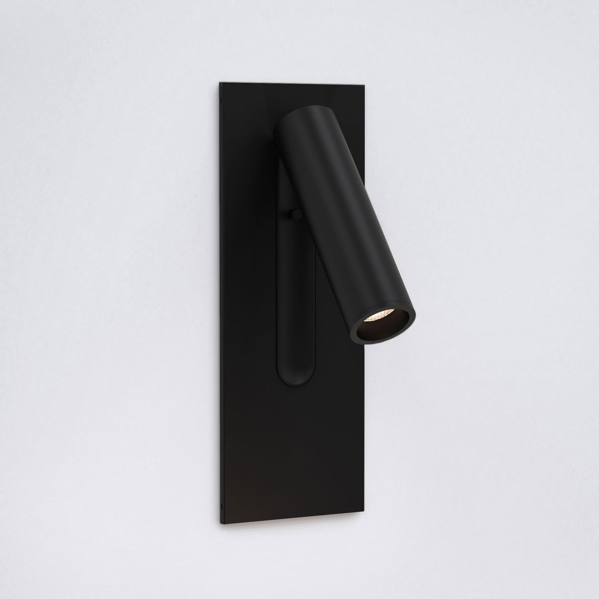 Black wall-mounted spotlight with a cylindrical head angled downwards, emitting a warm light