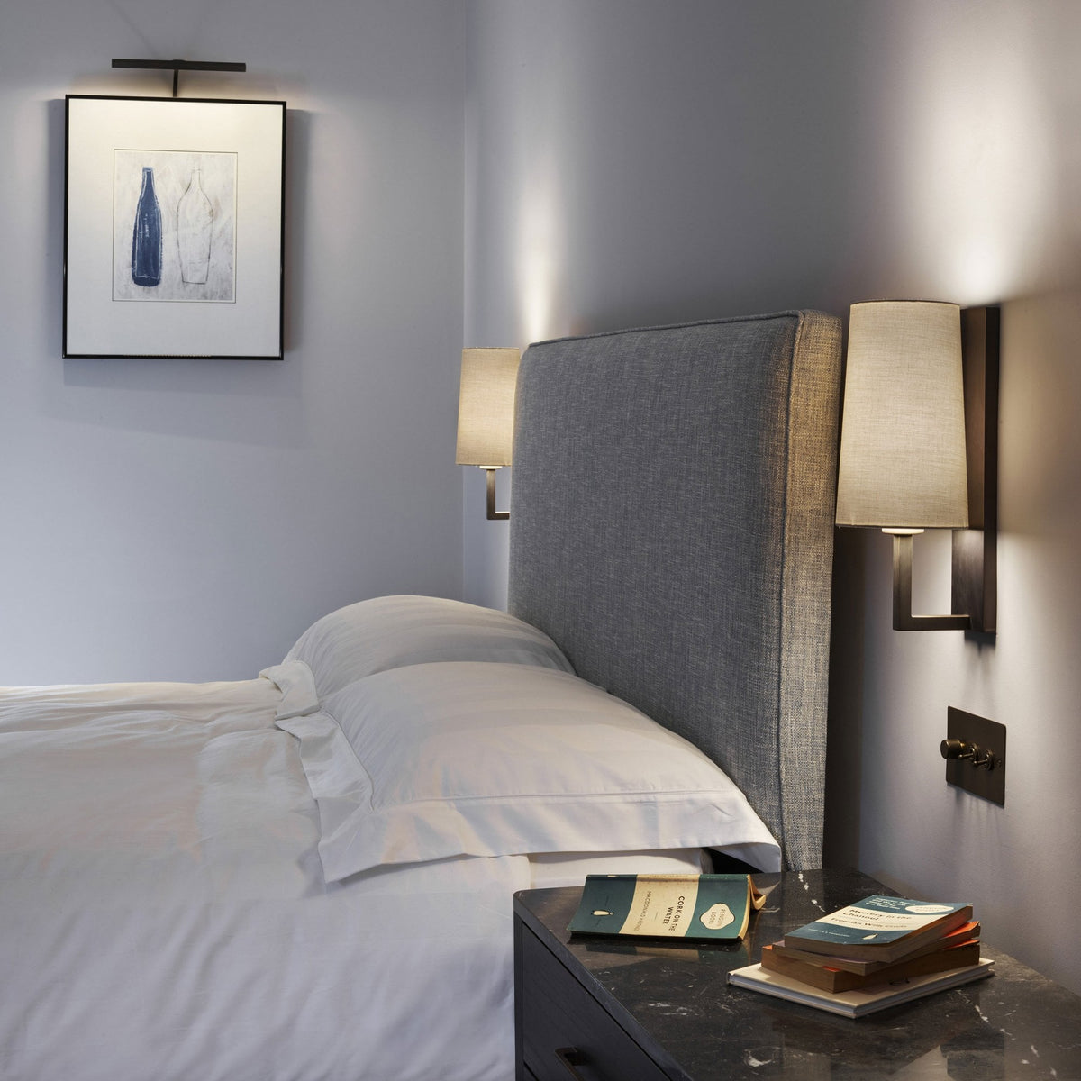 Bedroom with a grey upholstered headboard, white bedding, and two wall-mounted lamps