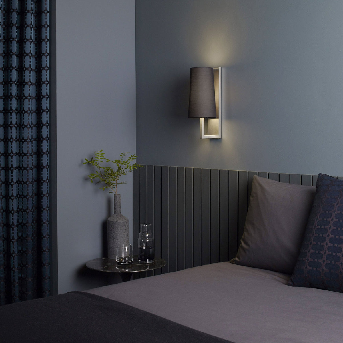 Bedroom with dark grey walls, a bed with grey bedding, and a wall-mounted lamp with a black shade