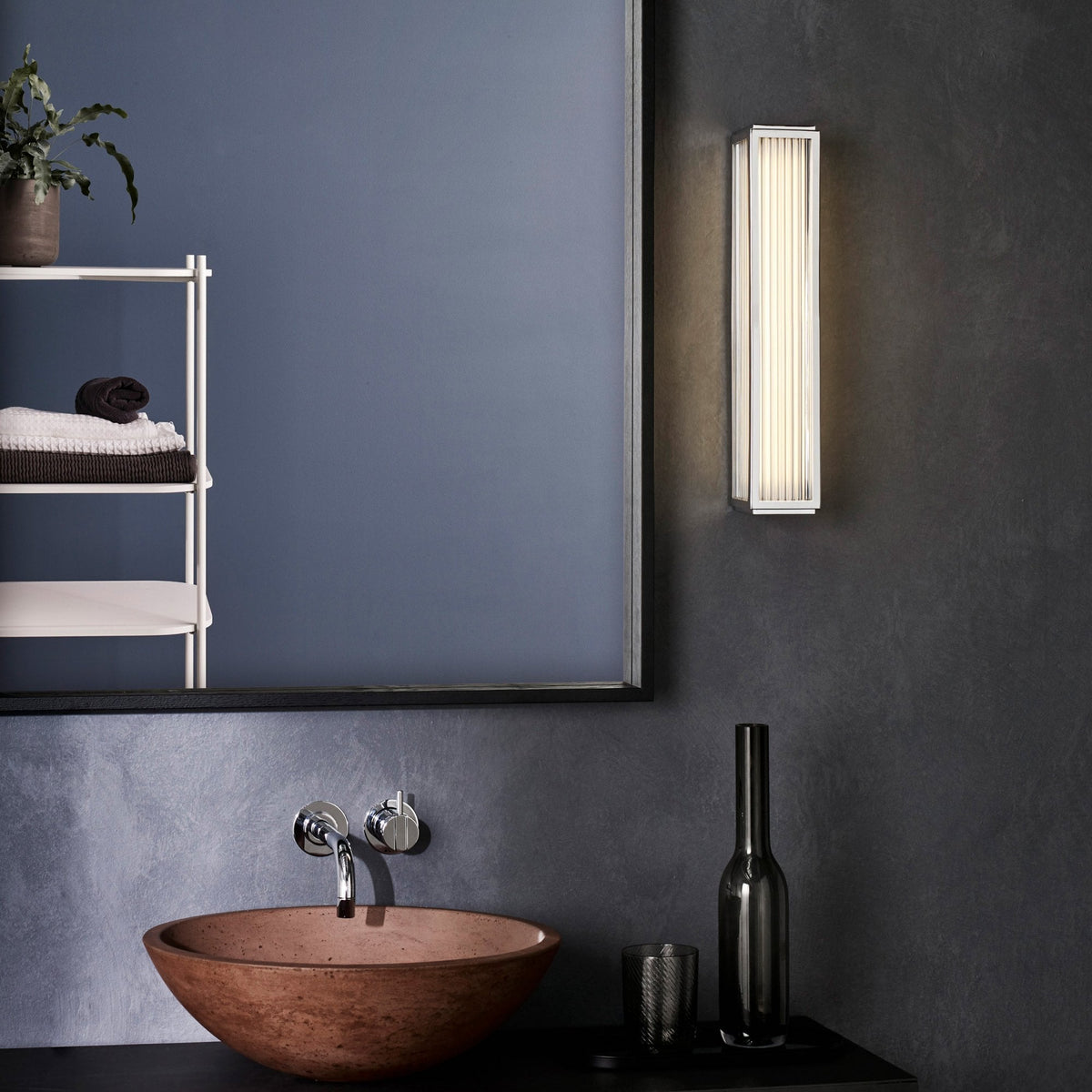 Bathroom interior with a terracotta sink, wall-mounted faucet, mirror, and a vertical ribbed wall light