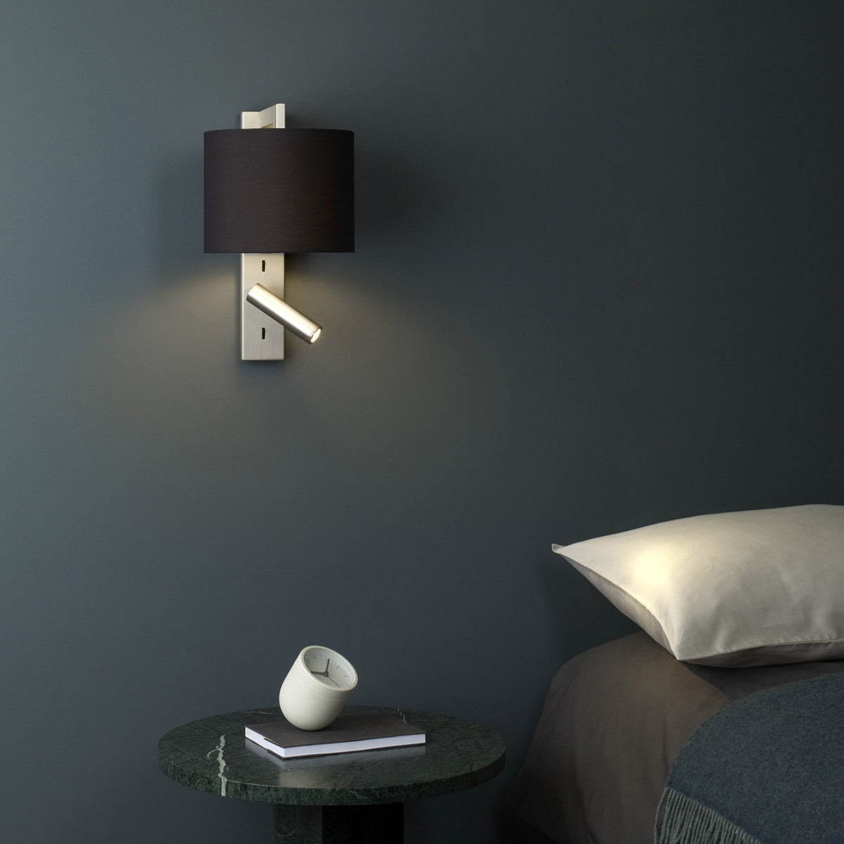 Wall-mounted lamp with black shade and adjustable reading light above a marble side table with a clock